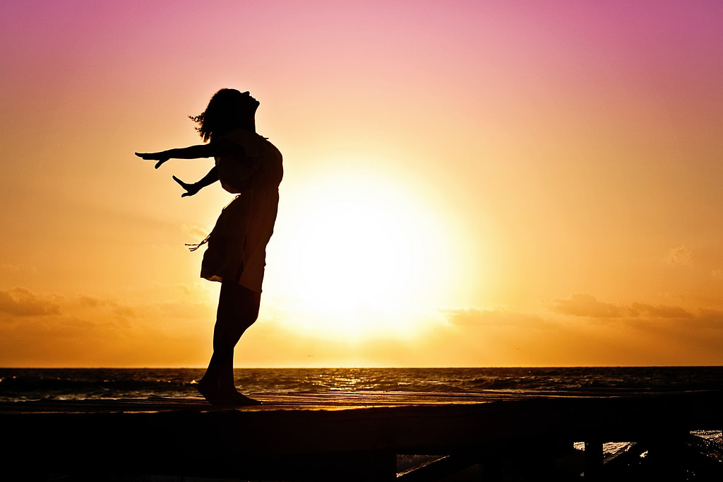 Femme debout bras écartés respirant au soleil levant Femme debout bras écartés respirant au soleil levant