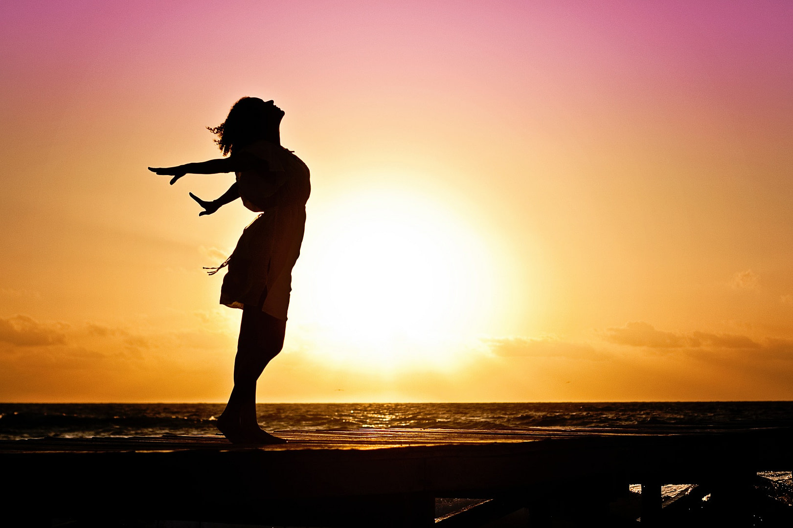 Femme debout bras écartés respirant au soleil levant